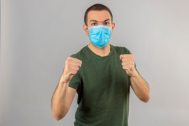 Молодой человек, носящий медицинскую маску с сердитым лицом, стоящую с боксерскими кулаками, и готовый атаковать, изолированный на белом