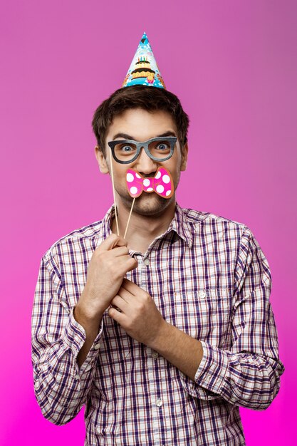 Young man wearing fake glasses and butterfly over purple wall.