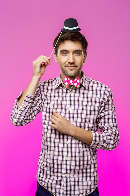 Young man wearing fake hat and butterfly over purple wall.