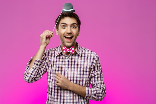 Young man wearing fake hat and butterfly over purple wall.