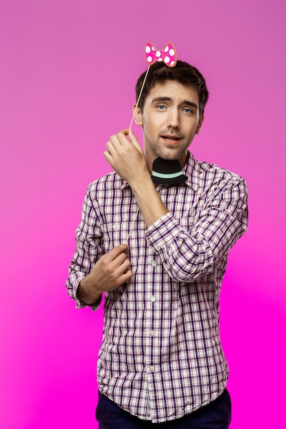 Young man wearing fake hat and butterfly over purple wall.