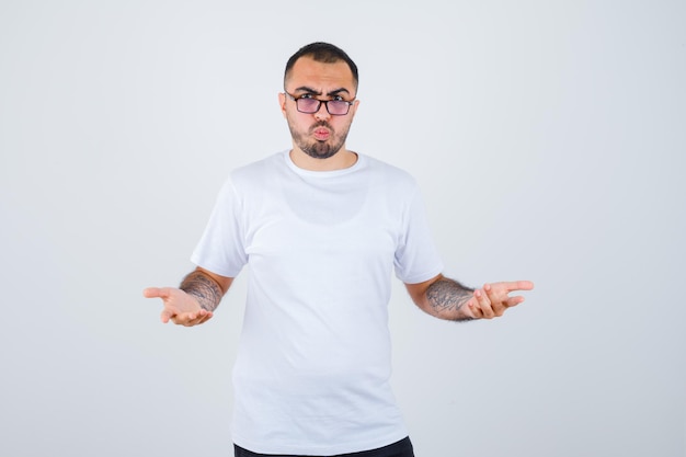 Young man wearing glasses and stretching hands as holding something in white t-shirt and black pants and looking serious