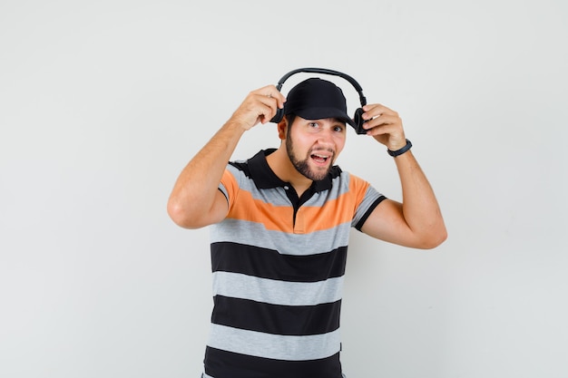 Young man wearing headphones in t-shirt, cap and looking merry.