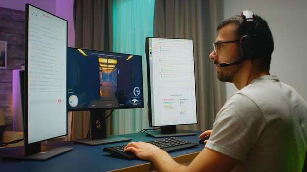 Young man wearing headphones talking with other players while playing professional shooter games in an online tournament