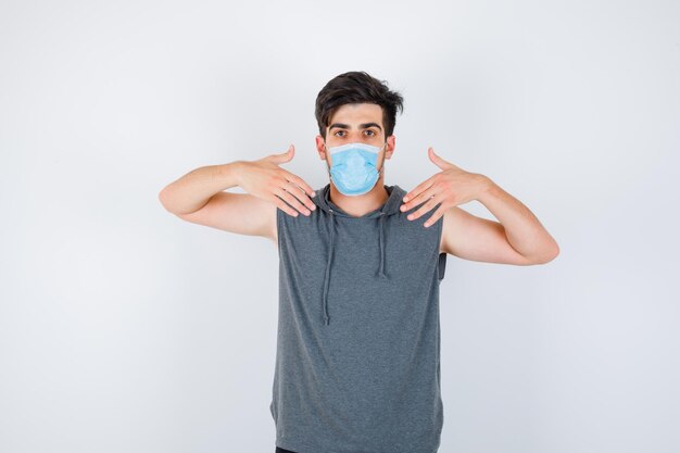 Young man wearing mask while pointing at himself in gray t-shirt and looking serious