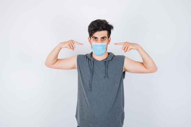 Young man wearing mask while pointing himself in gray t-shirt and looking serious