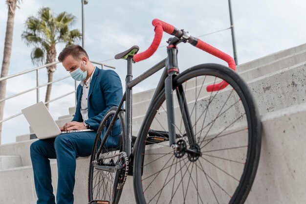 彼の自転車の隣に座っている間医療マスクを身に着けている若い男