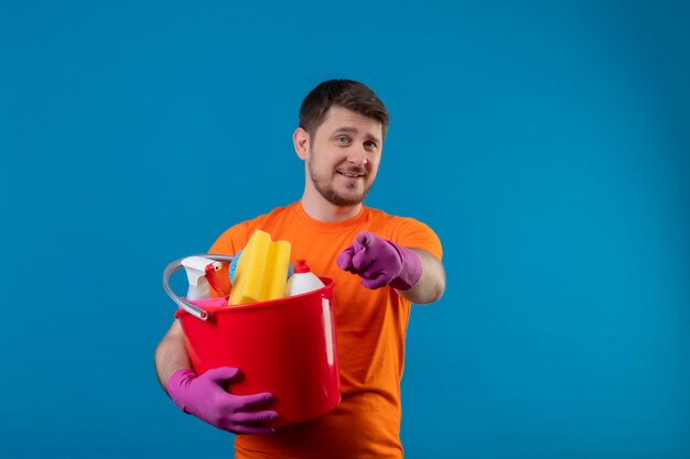 청소 도구와 양동이를 들고 오렌지 티셔츠와 고무 장갑을 끼고 젊은 남자