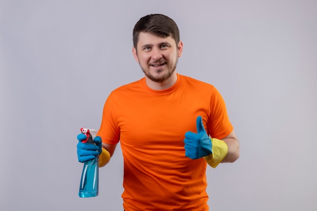 Молодой человек в оранжевой футболке и резиновых перчатках держит чистящий спрей улыбается