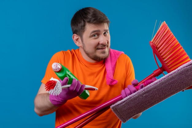 Young man wearing orange t-shirt and rubber gloves holding cleaning tools