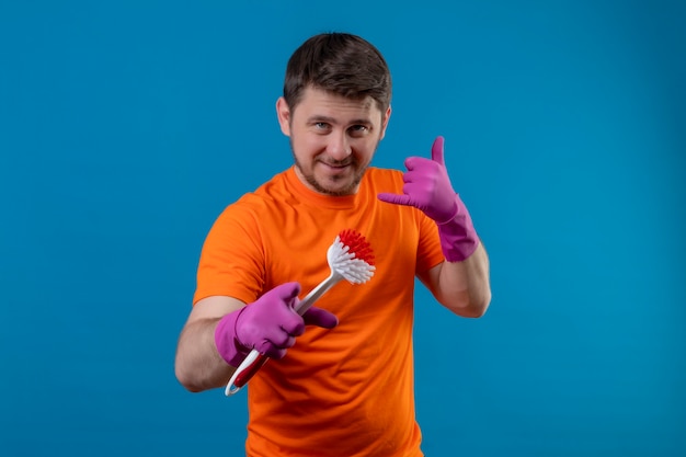 Young man wearing orange t-shirt and rubber gloves holding scrubbing brush
