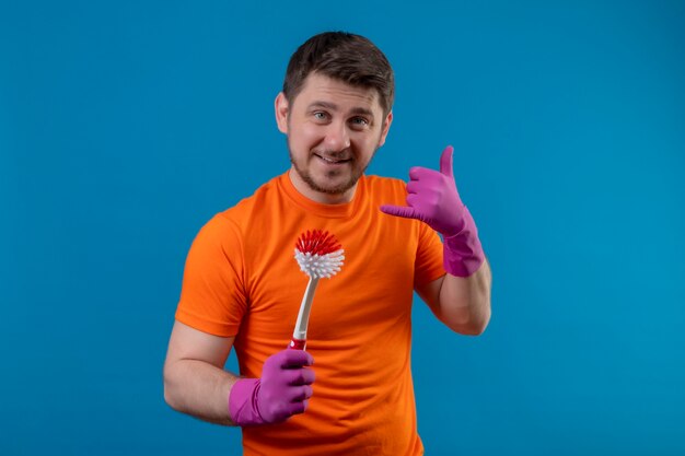 Young man wearing orange t-shirt and rubber gloves holding scrubbing brush
