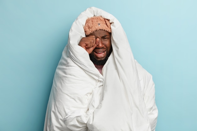 Young man wearing sleep mask and wrapped in white blanket