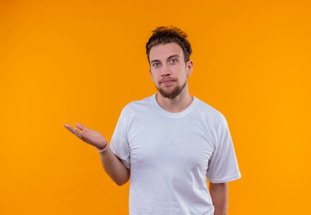  young man wearing white t-shirt holding hand out at side on isolated orange wall