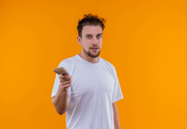 young man wearing white t-shirt holding out paint brush on isolated orange wall