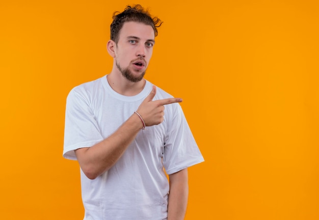  young man wearing white t-shirt points to side on isolated orange wall