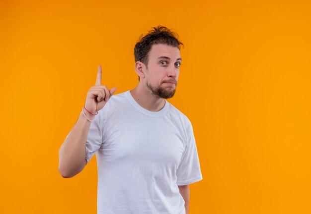 白いTシャツを着ている若い男は、孤立したオレンジ色の壁の上を指しています