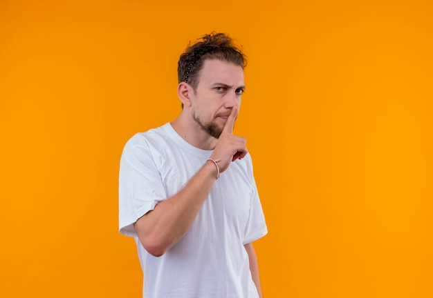  young man wearing white t-shirt showing silence gesture on isolated orange wall