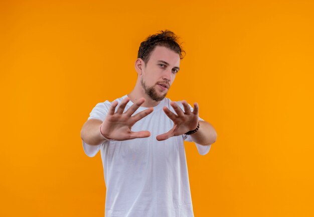 孤立したオレンジ色の壁に停止ジェスチャーを示す白いTシャツを着て若い男