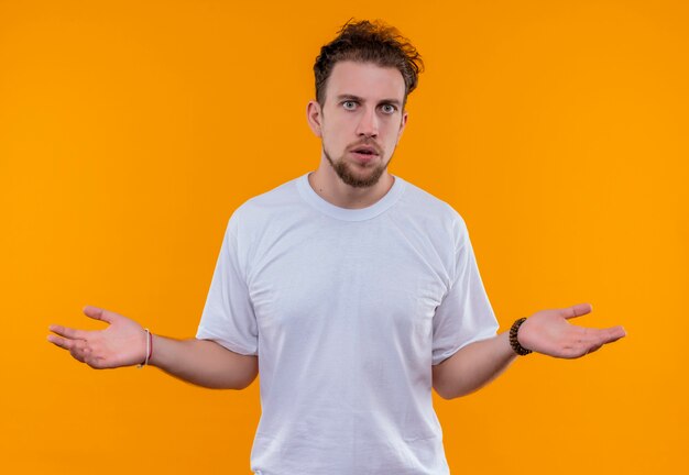 孤立したオレンジ色の壁にどのようなジェスチャーを示す白いTシャツを着ている若い男
