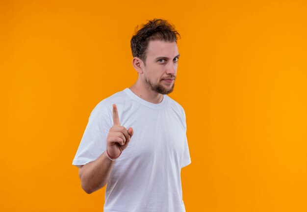 격리 된 오렌지 벽에 제스처를 보여주는 흰색 티셔츠를 입고 젊은 남자