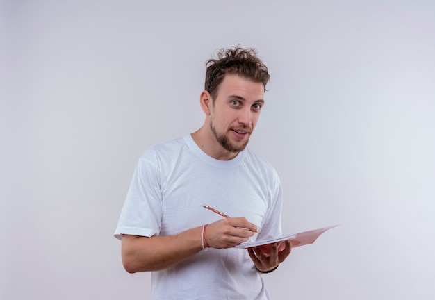  young man wearing white t-shirt writing something on notebook on isolated white wall