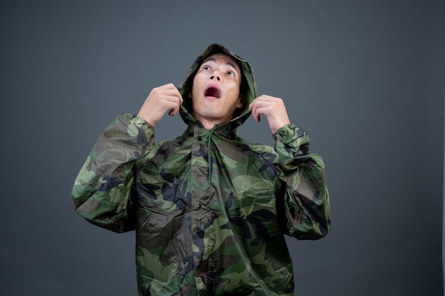 The young man wears a camouflage raincoat and shows different gestures. 