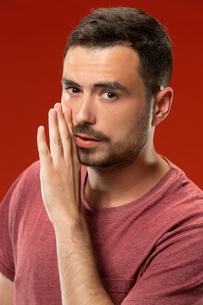 The young man whispering a secret behind her hand over red wall