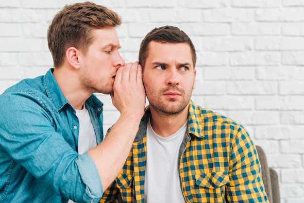 Premium Photo Young Man Whispering A Secret In His Friend S Ear