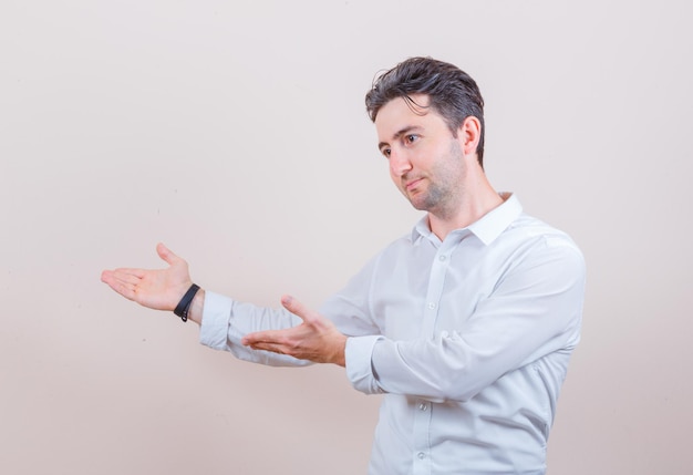 Young man in white shirt doing welcome gesture and looking gentle