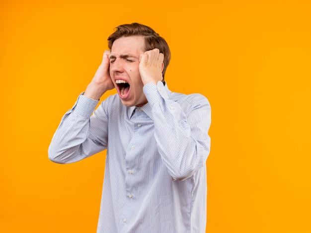 Young man in white shirt frustrated angry with aggressive expression standing over orange wall