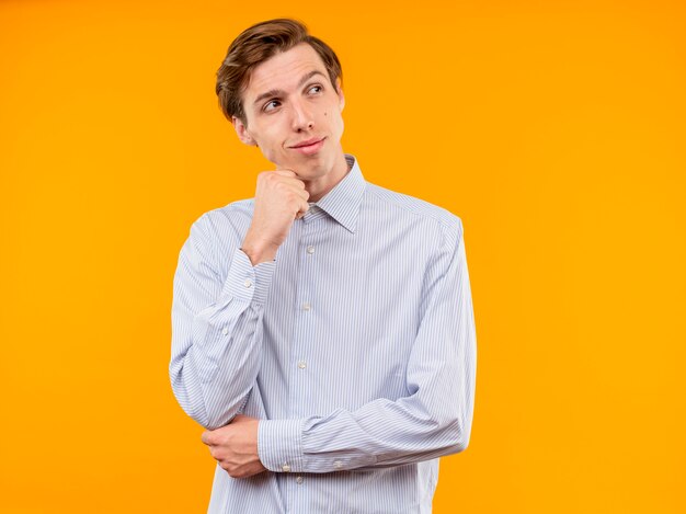 Young man in white shirt looking aside with smile on face standing over orange wall