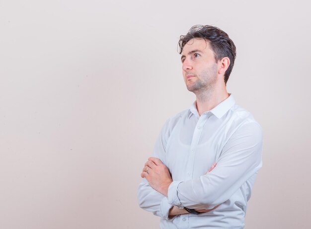 Young man in white shirt looking up with crossed arms and looking thoughtful