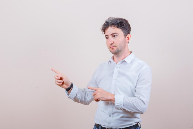 Young man in white shirt pointing away and looking pensive