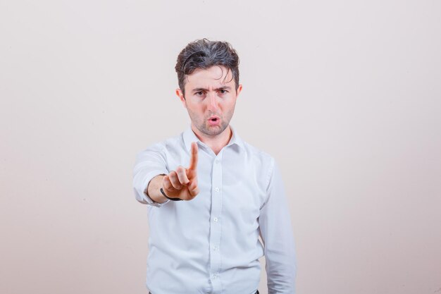 Young man in white shirt showing hold on a minute gesture and looking serious