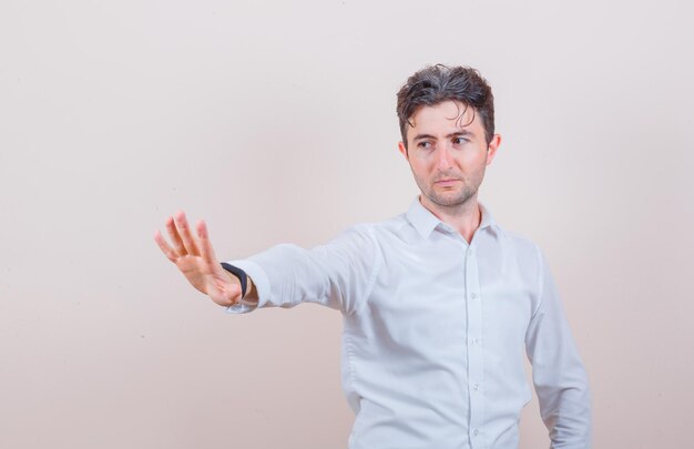 Young man in white shirt showing stop gesture and looking focused