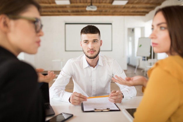 Молодой человек в белой рубашке задумчиво смотрит на работодателей, проводя время в современном офисе