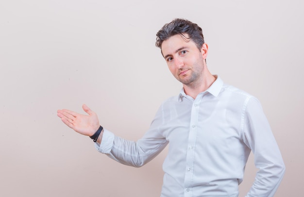 Young man in white shirt welcoming or showing something and looking gentle