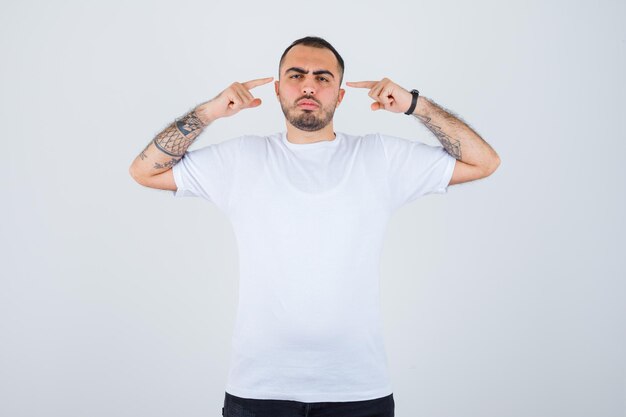 Young man in white t-shirt and black pants pointing ears and looking serious