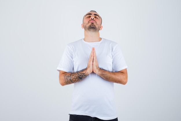 Free photo young man in white t-shirt and black pants showing namaste gesture and looking serious