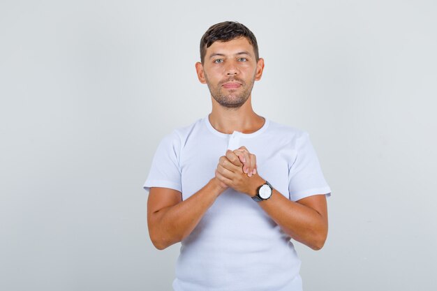 Young man in white t-shirt clasping hands clenched together, front view.