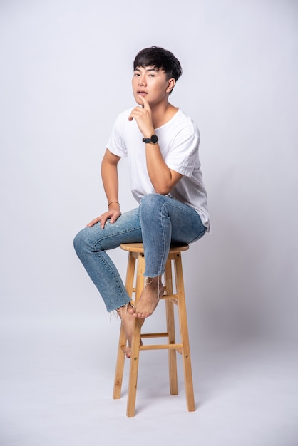 A young man in a white T-shirt is sitting on a high chair.