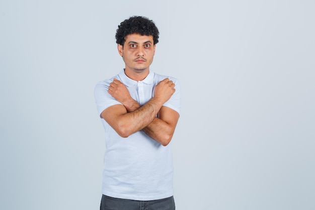 Young man in white t-shirt and jeans showing x or restriction gesture and looking serious , front view.