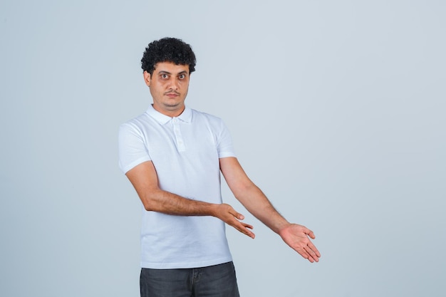 Young man in white t-shirt and jeans stretching hands down and looking serious , front view.