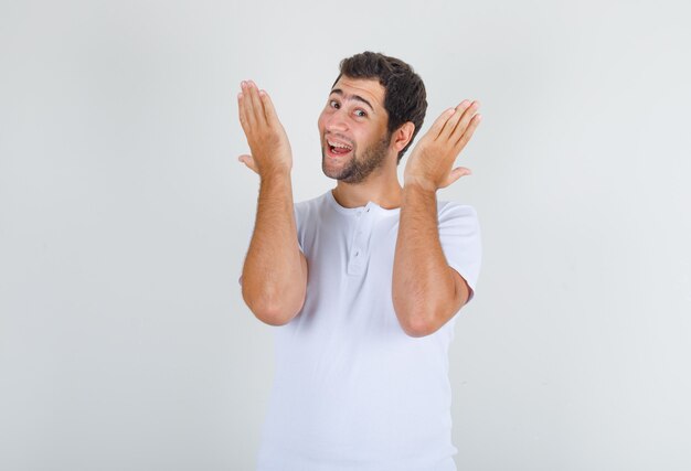 Young man in white t-shirt lifting palms and shaking hands and looking cheery