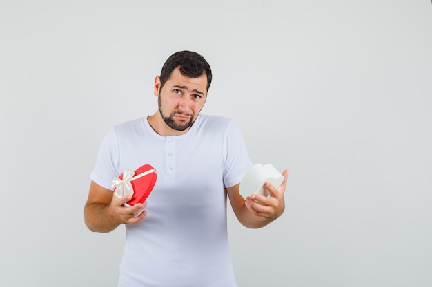 Young man in white t-shirt looking into present box and looking sad , front view.