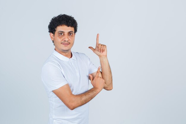 Young man in white t-shirt showing gun gesture and looking confident , front view.