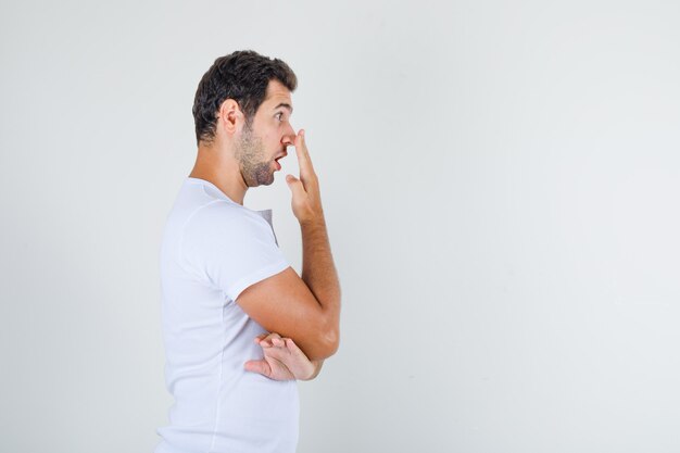 手で鼻に触れると見てみるとビックリの白いtシャツの若い男。