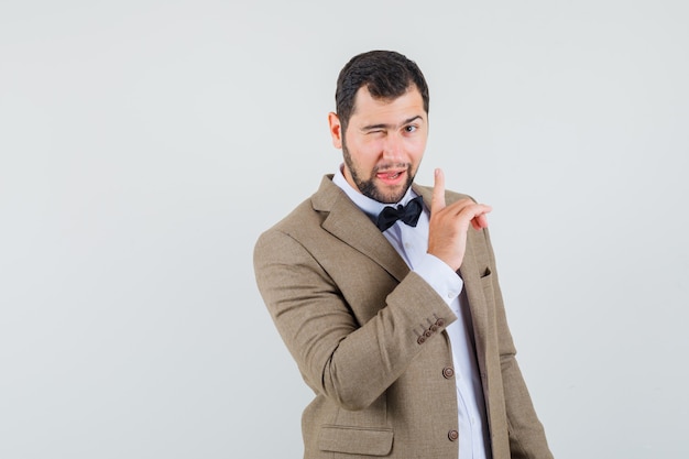 Young man winking eye and showing silence sign in suit , front view.