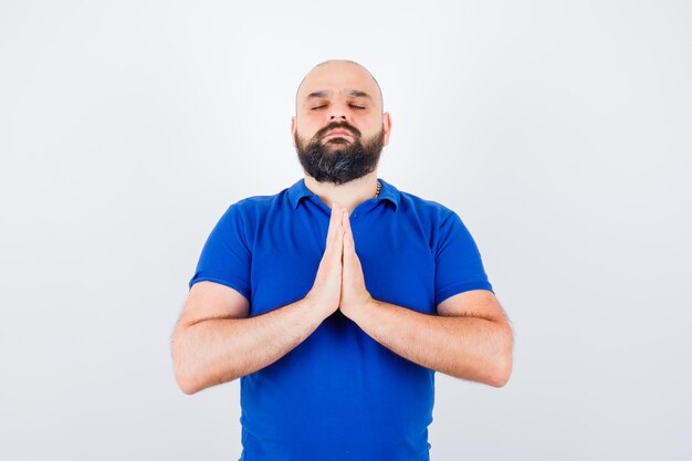 Young man wishing in blue shirt and looking hopeful. front view.